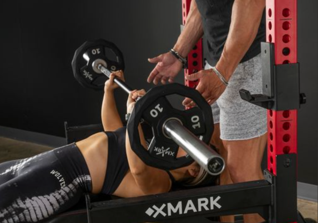 Woman Bench pressing while man spots her