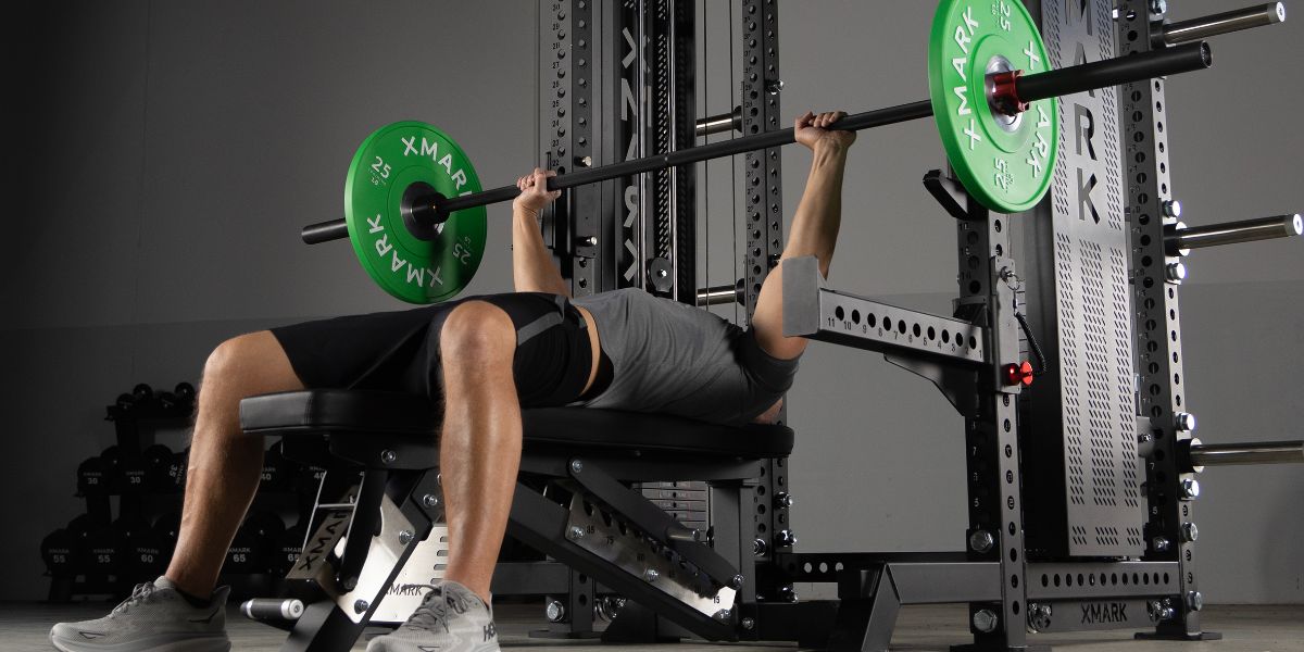 Man bench pressing with XMARK green plates inside of an XMARK Power Rack