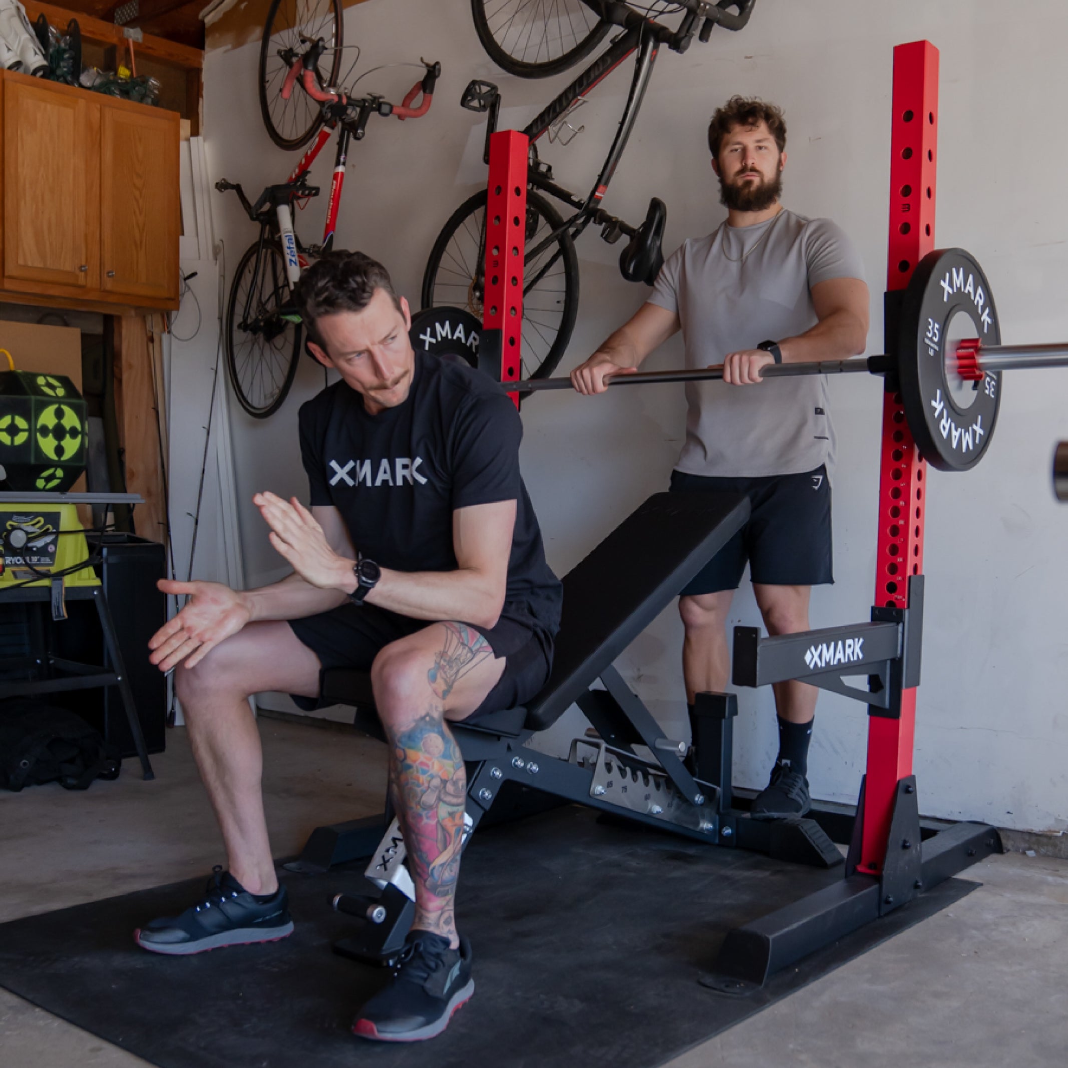 Man sitting on xmark adjustable bench between sets with a spotter