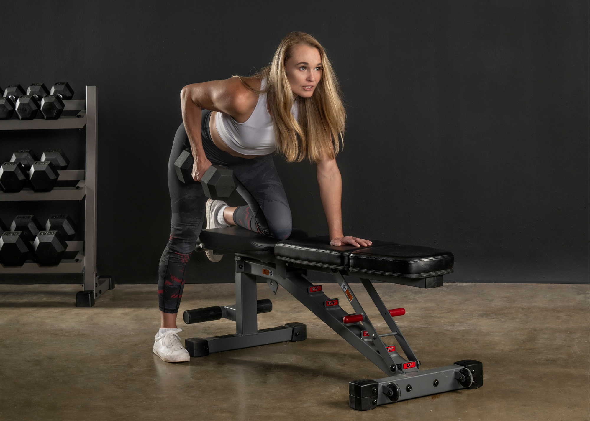 Female propped on weight bench while doing upper body dumbbell exercises.