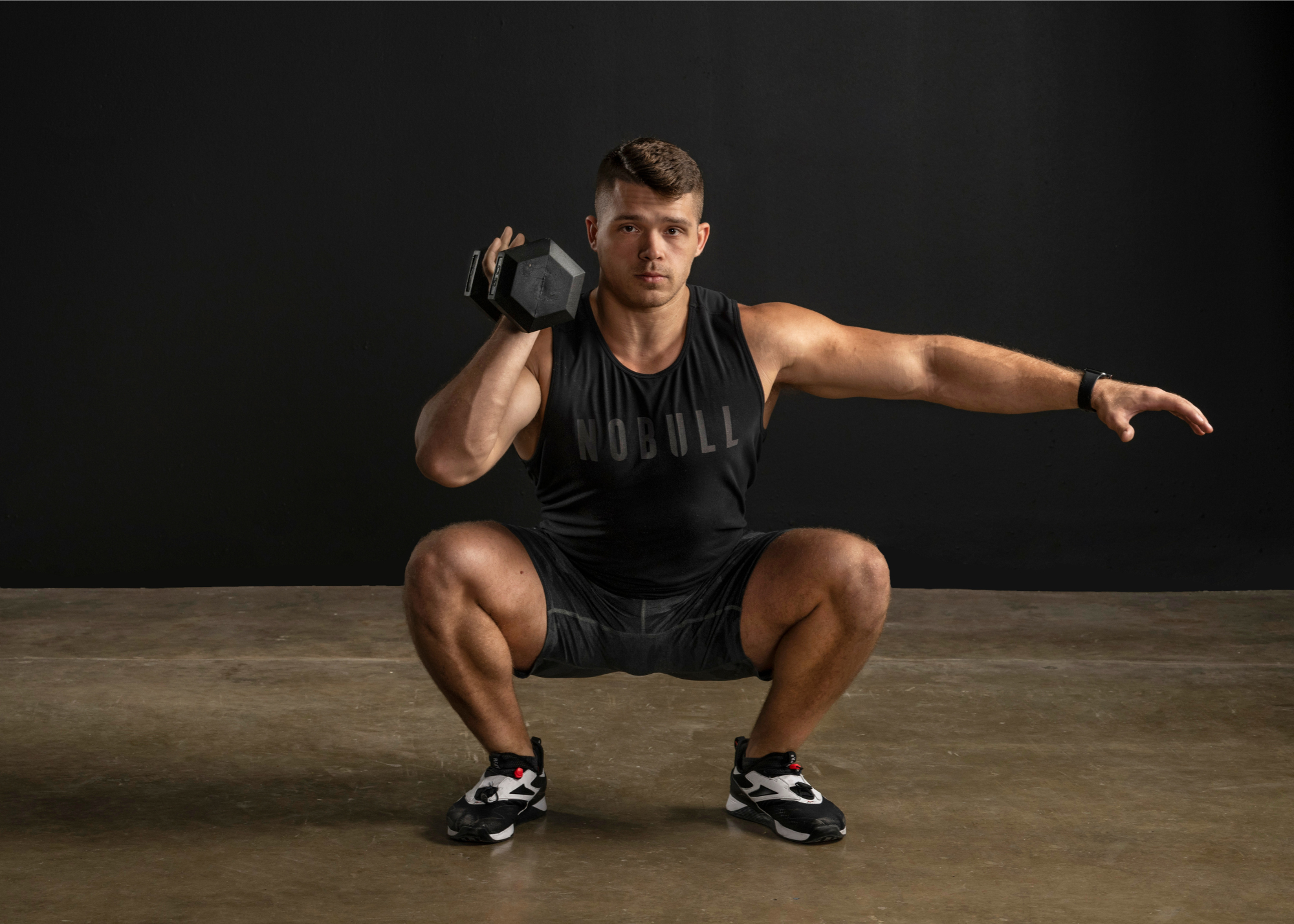 Male in squat position while doing a right arm bicep curl using a hex dumbbell.