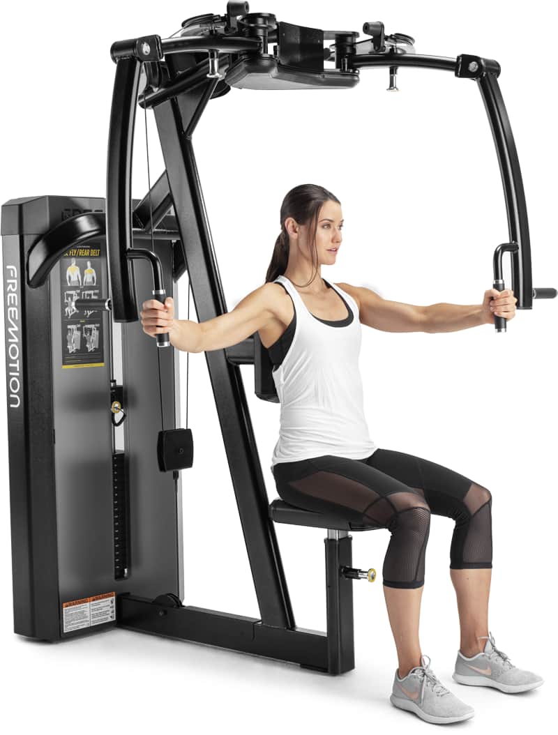 A woman in a white tank top and black leggings is using a Freemotion cable chest exercise machine on a solid white background.