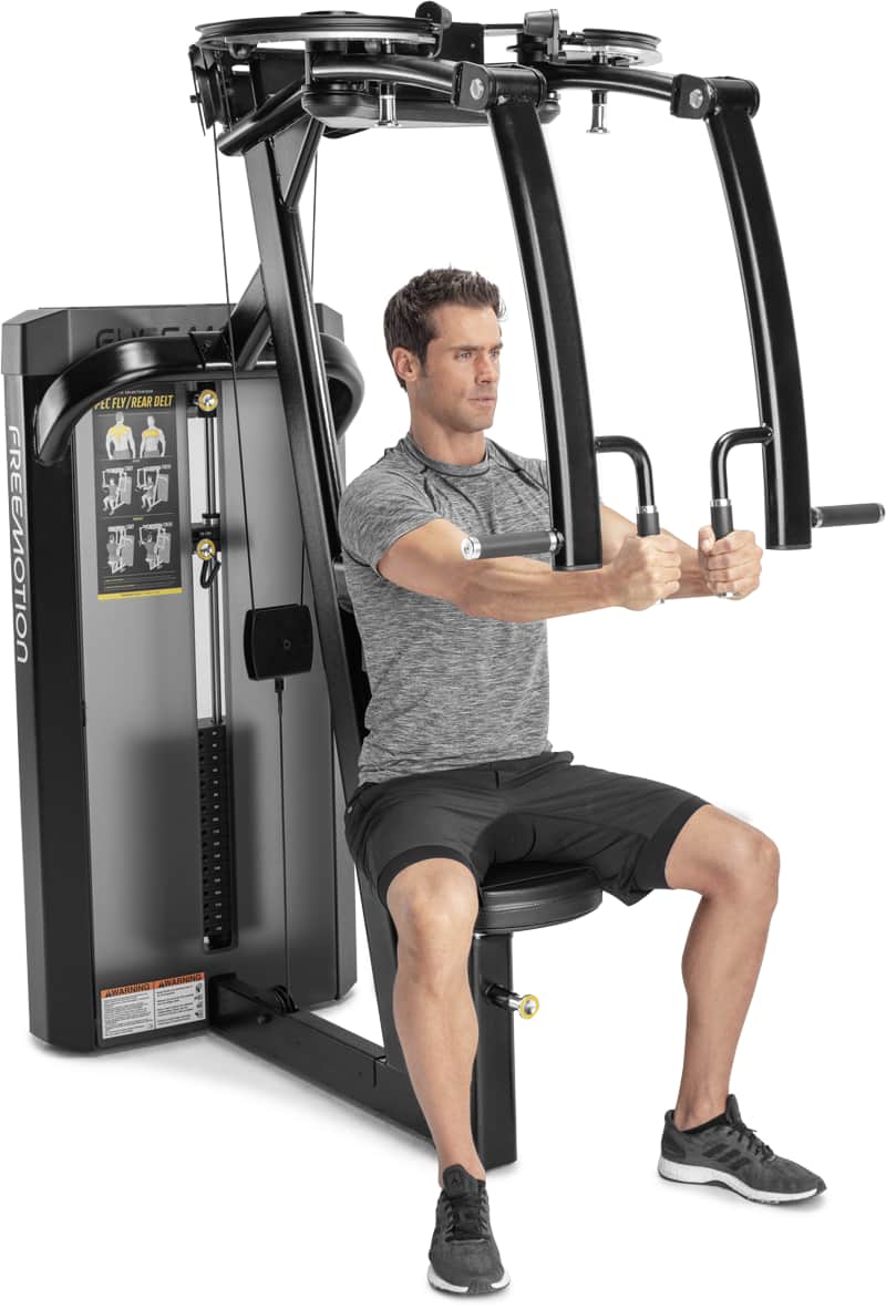 A man wearing a gray t-shirt and black shorts is seated on a chest extension machine, demonstrating its use.
