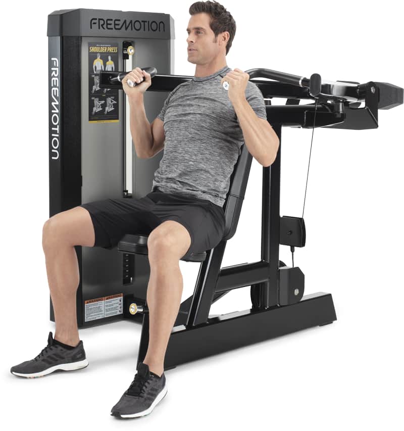 A man seated on a FREEMOTION chest press exercise machine, demonstrating use of the weight machine against a clean white background.